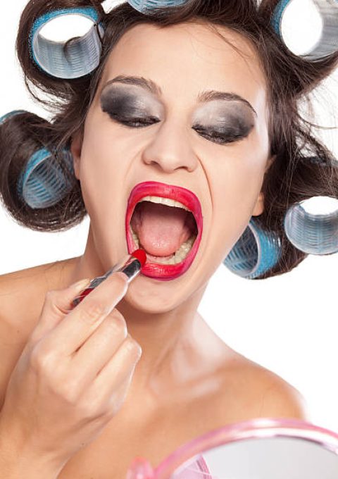 Funny woman with curlers and bad makeup applying lipstic