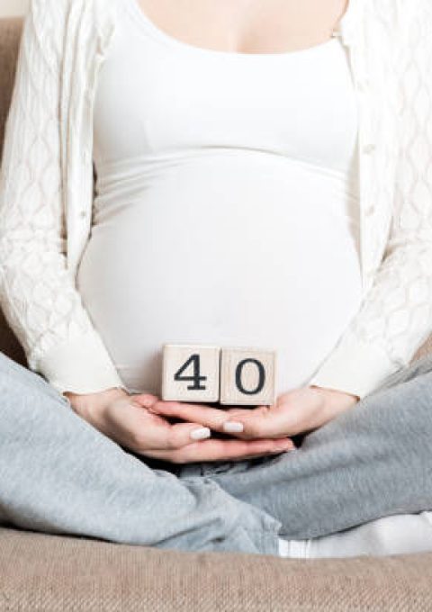 Pregnant woman in white underwear on bed in home holding calendar with weeks 40 of pregnant. Maternity concept. Expecting an upcoming baby.